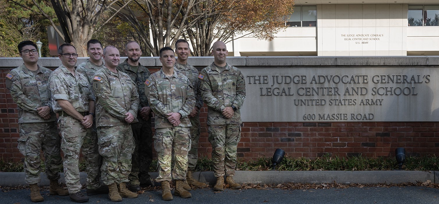 Soldiers standing in front of the TJAGLCS building sign